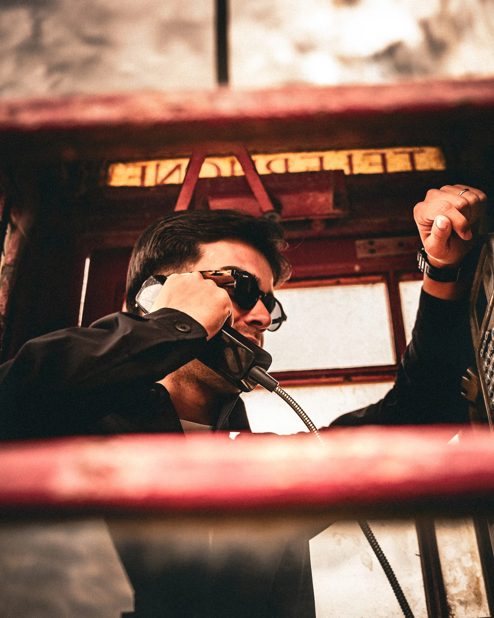 Cinematic portrait of a man leaning out of a red telephone box at sunset