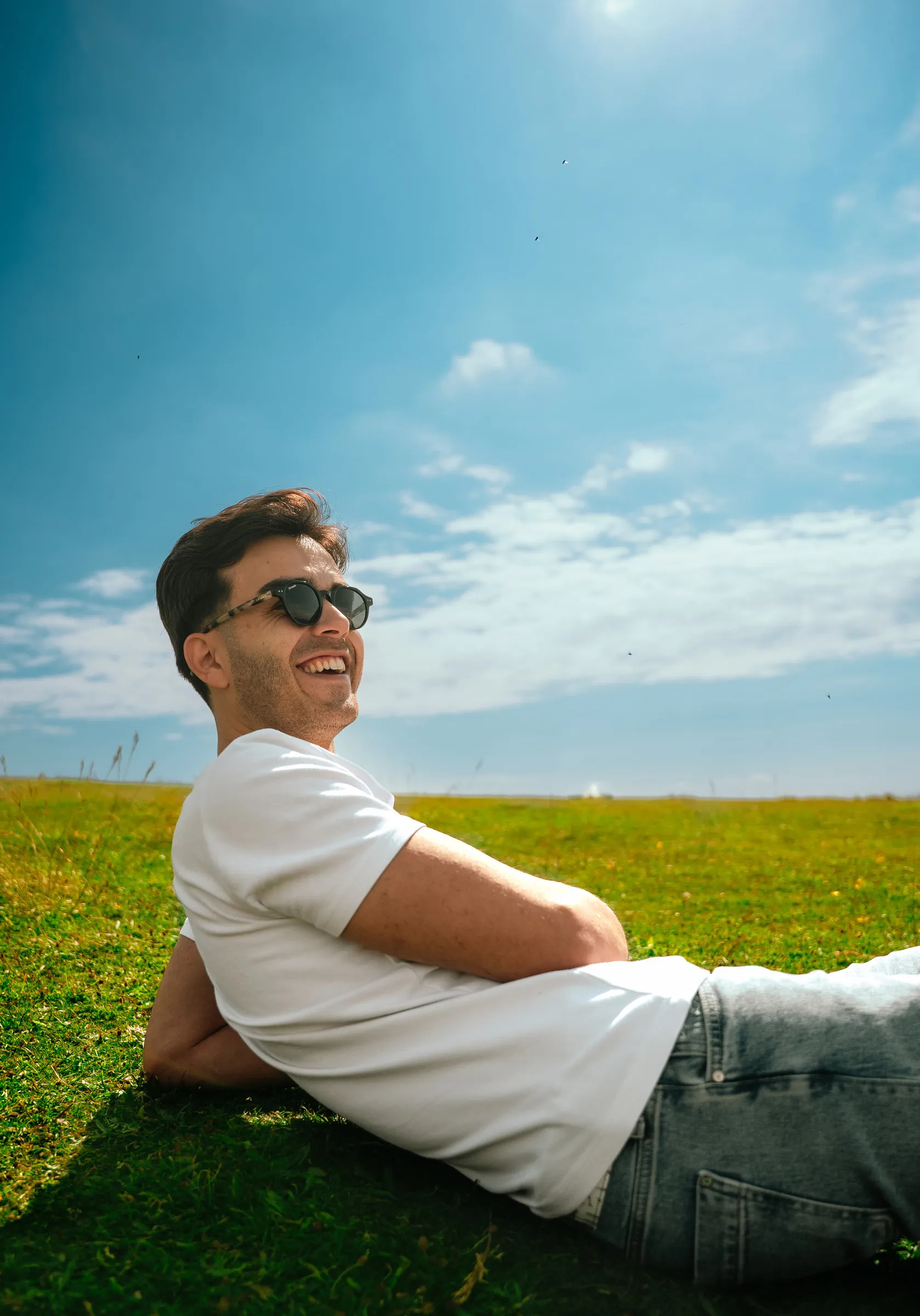 A man reclining on the grass on a bright summer day, sky overhead