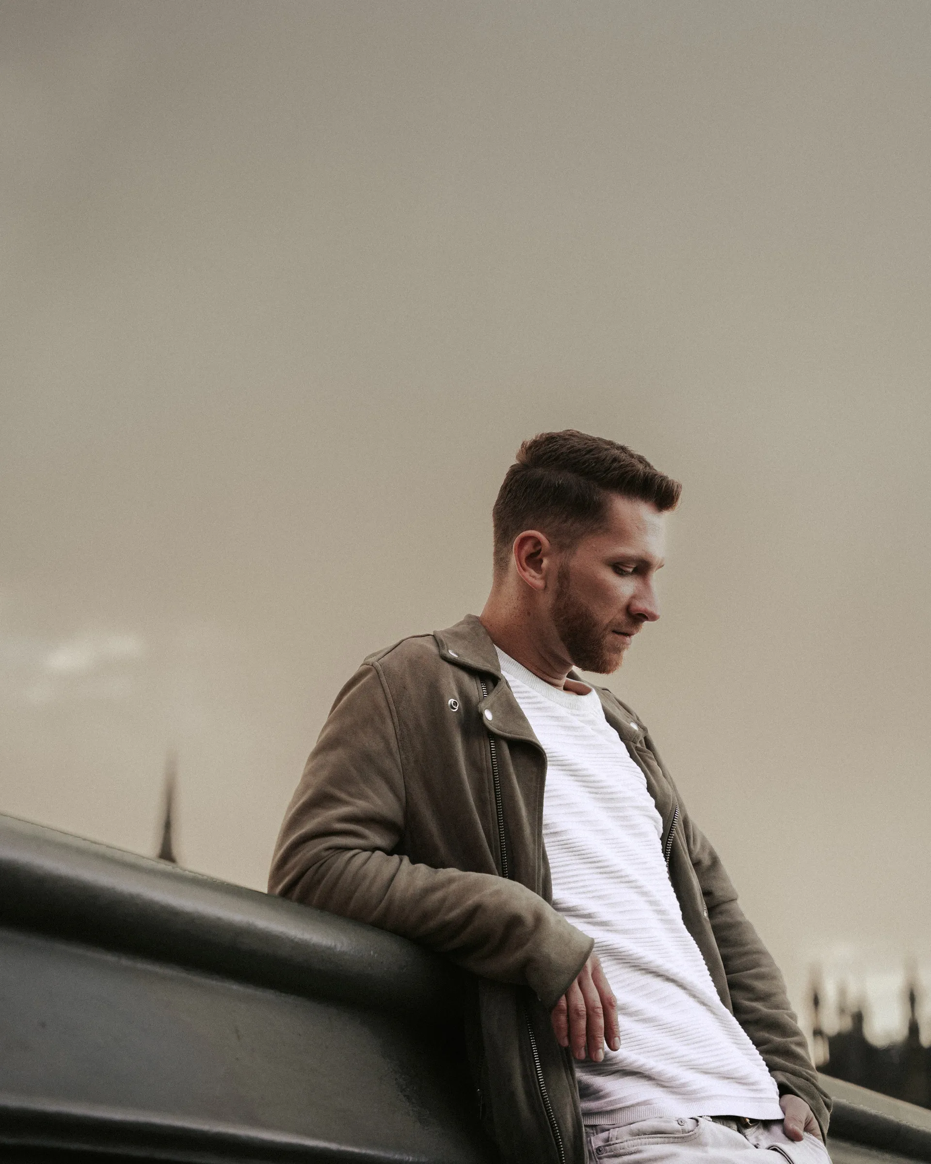 A man resting against a bridge parapet under a soft grey sky