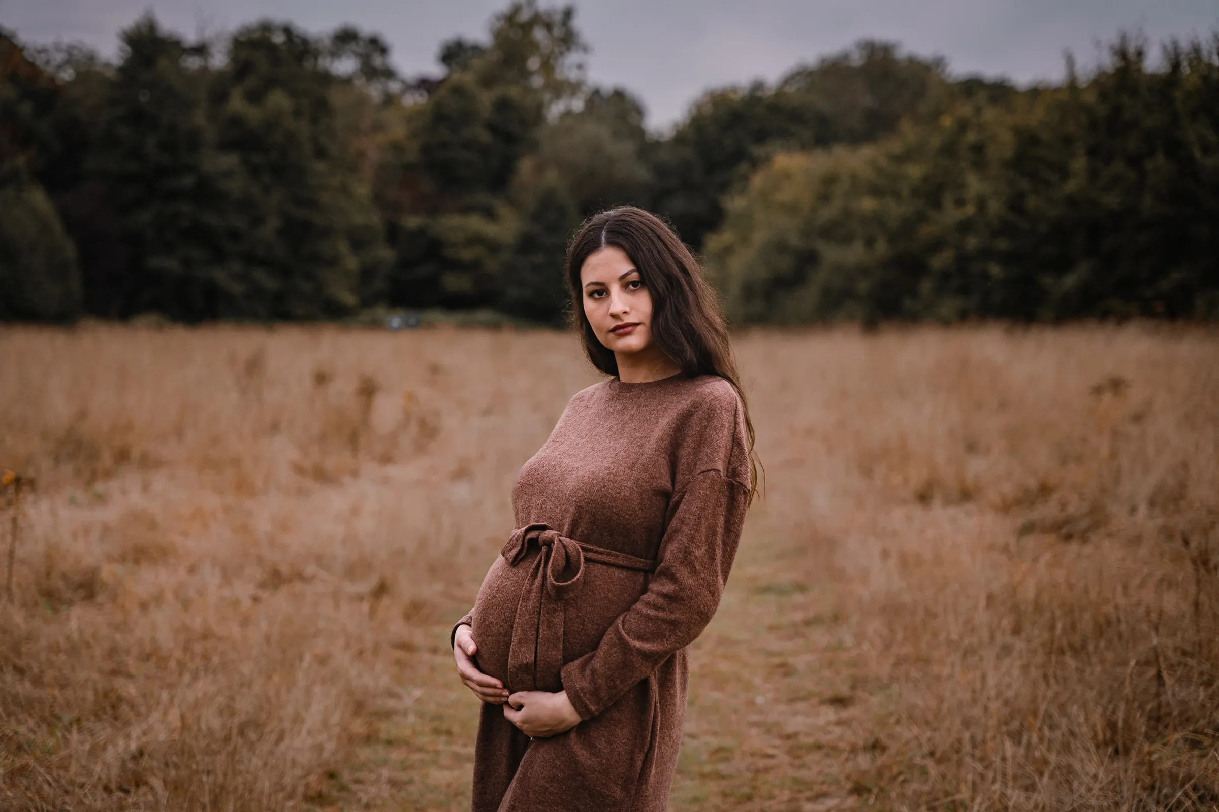 Maternity portrait in a field of tall golden grass at dusk