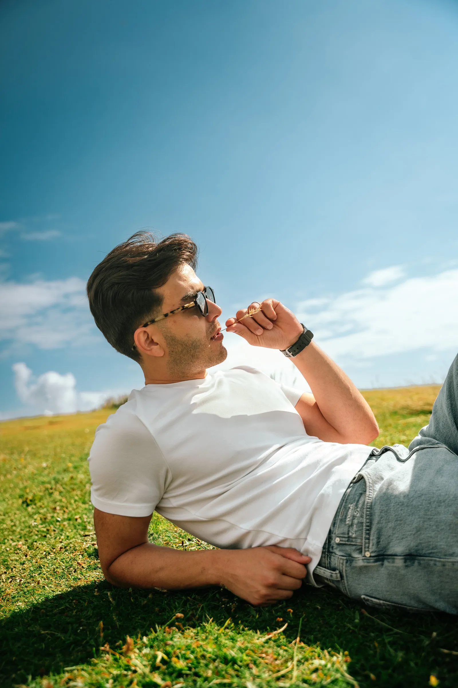 A man lying back on the grass against a deep blue summer sky