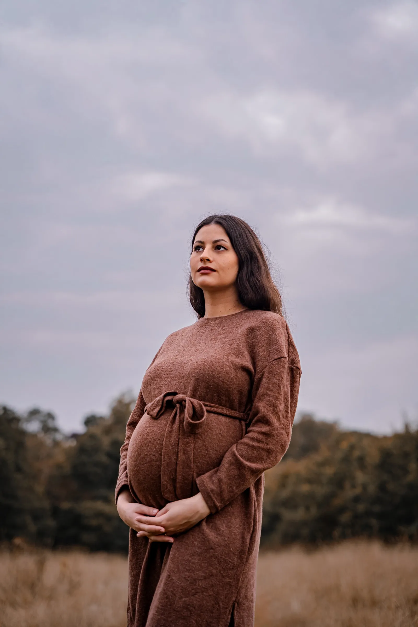 Maternity portrait in open meadow grass under a moody sky