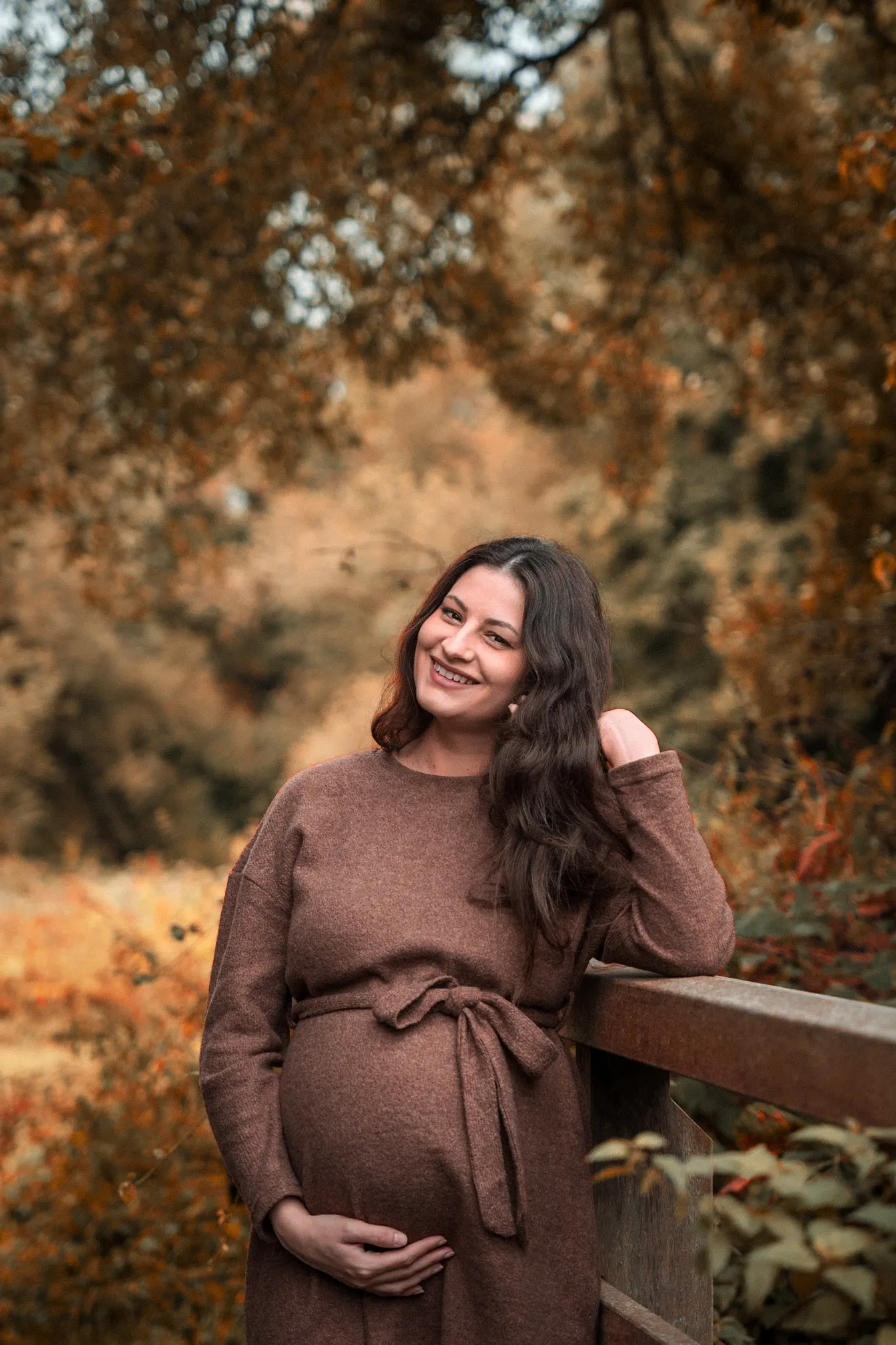 Maternity portrait leaning on a wooden fence surrounded by autumn foliage