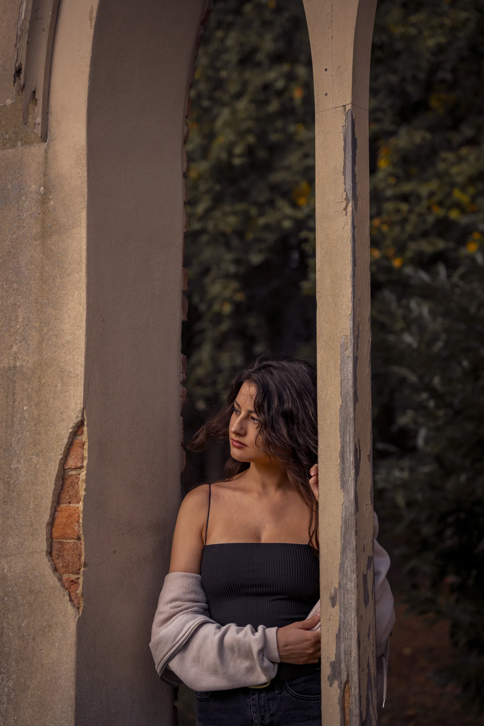 A woman resting against a weathered stone pillar in dappled light