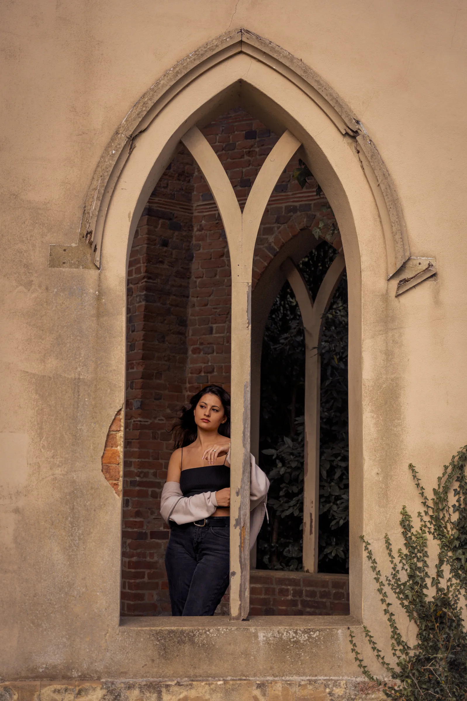 A woman standing inside a pointed gothic window of a ruined church