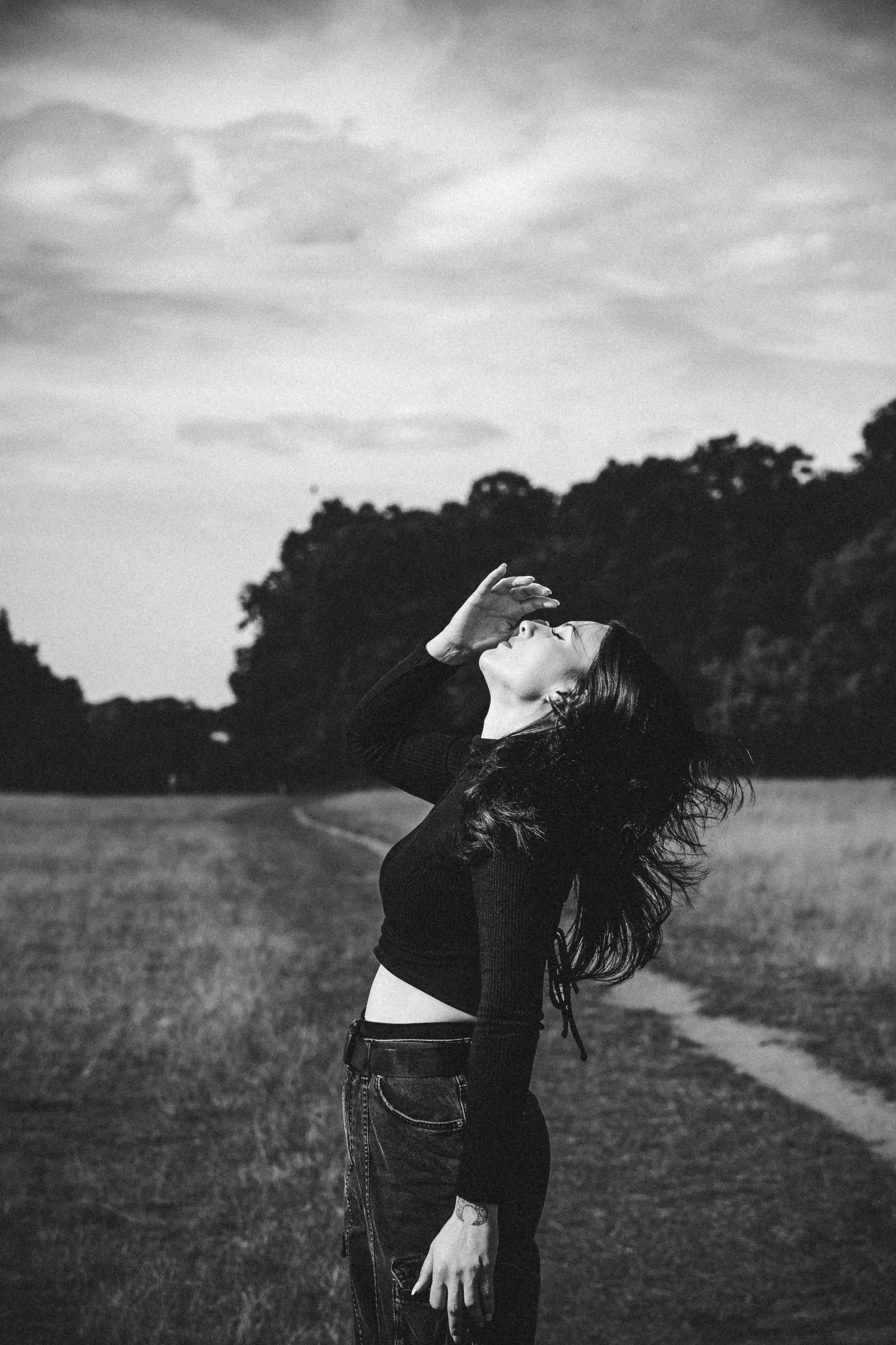 Black and white portrait of a woman on a country path, hair caught by the wind