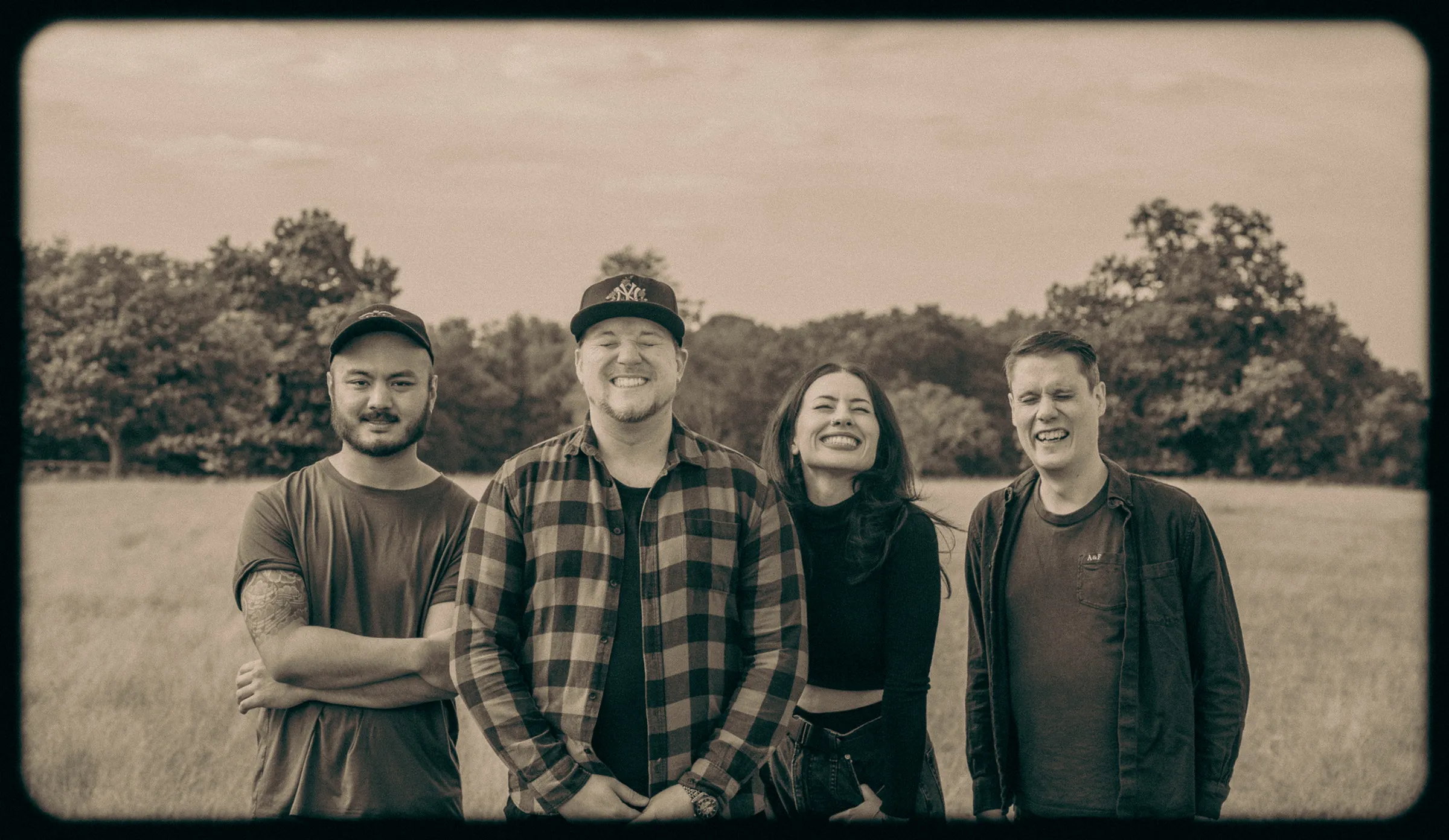 Sepia group portrait of a four-piece band standing in an open field