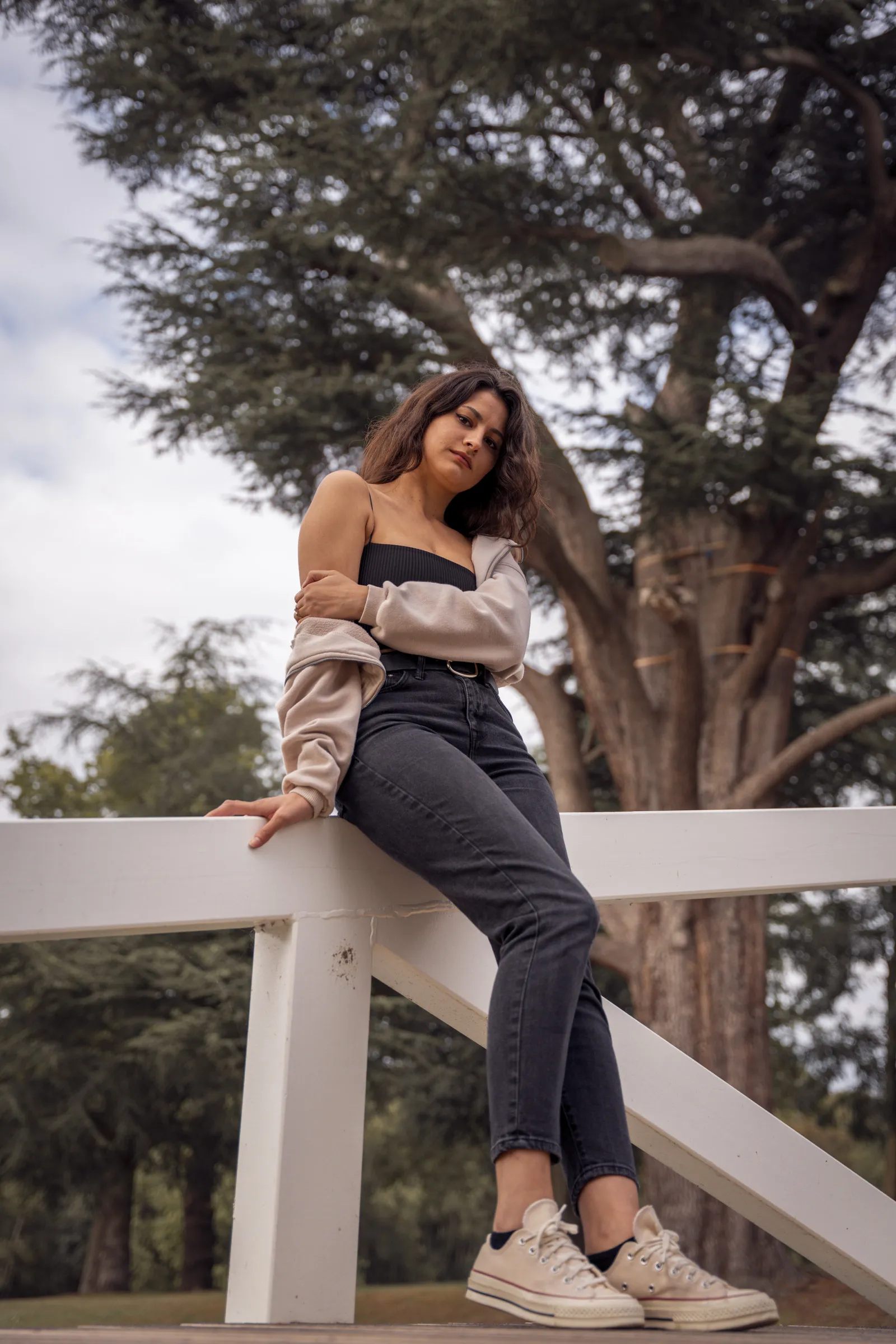 A woman seated on a white park railing beneath tall trees