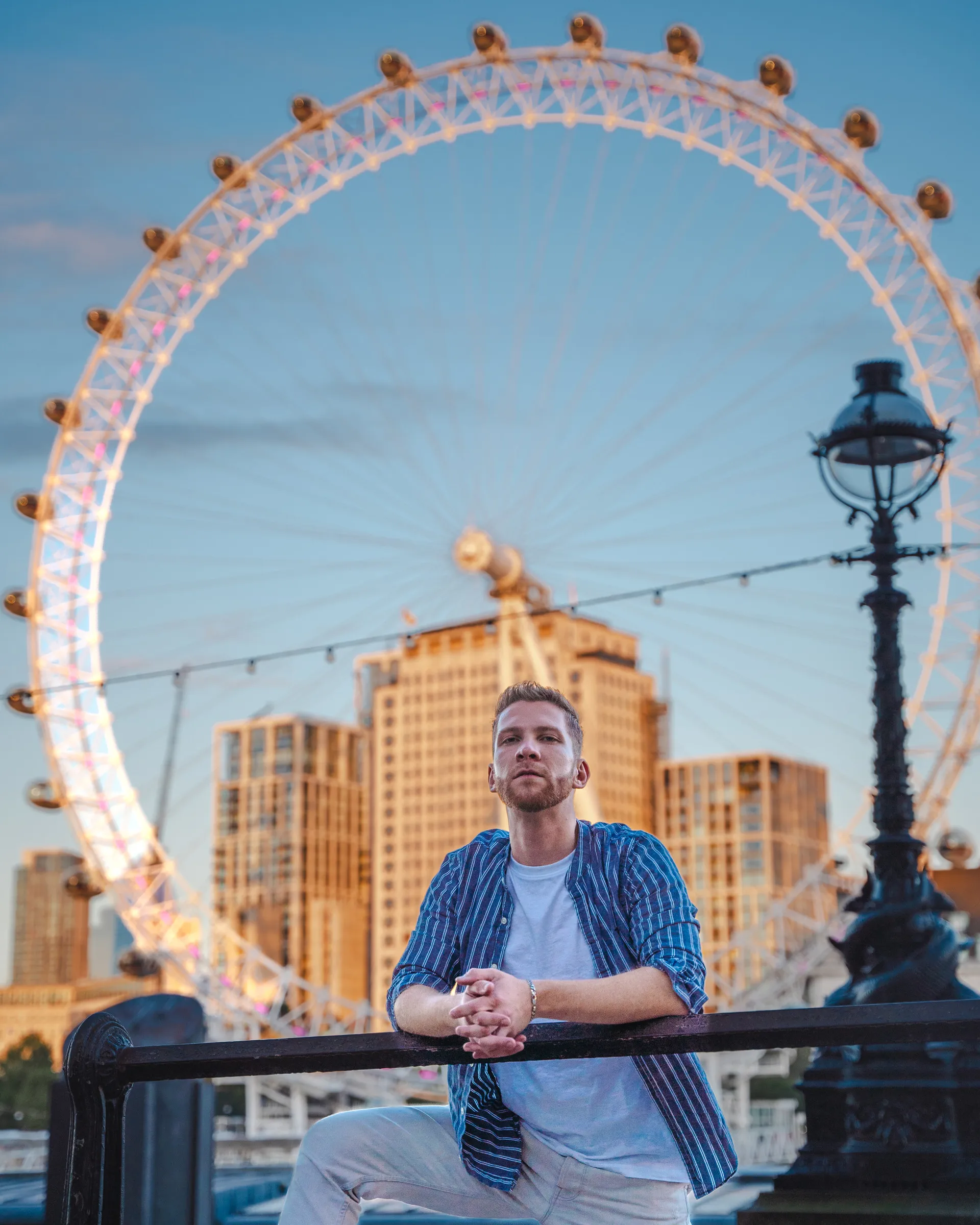 A man leaning on the river wall with the London Eye behind him at golden hour
