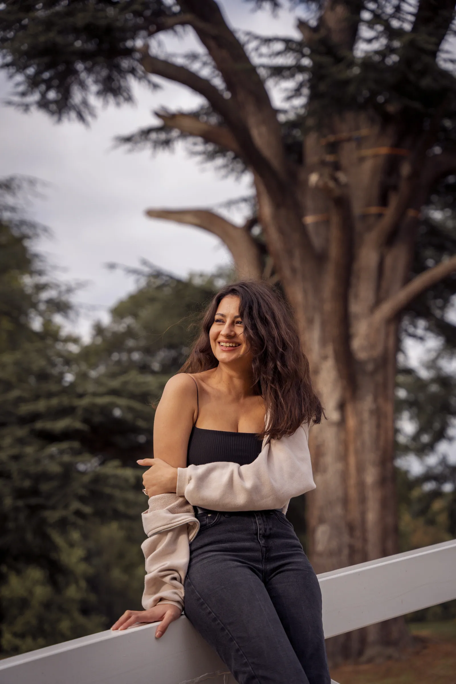 A woman perched on a fence rail beneath a broad tree canopy