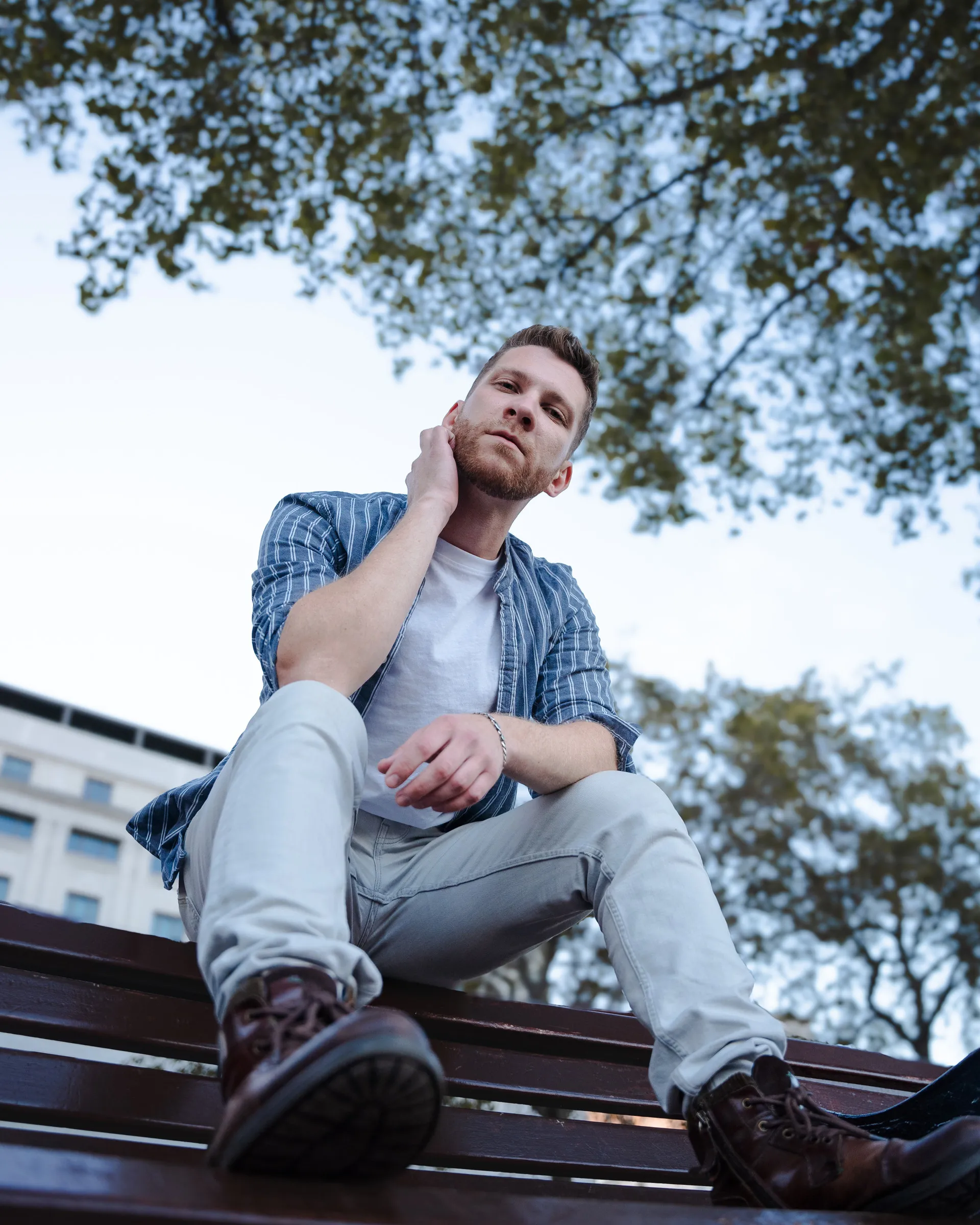 Low-angle portrait of a man sitting on a bench, trees and sky above