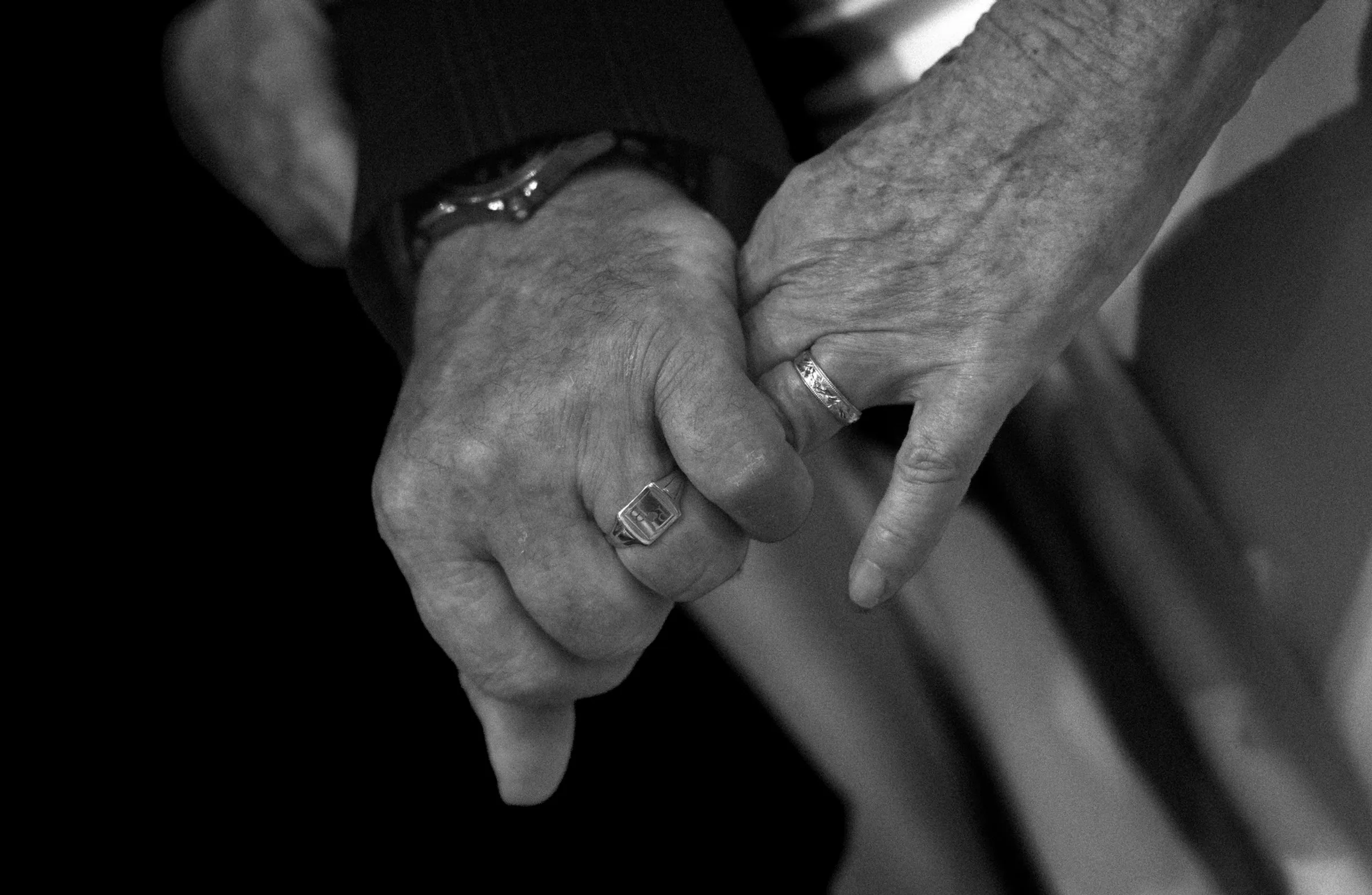 Close-up of the newlyweds holding hands, wedding rings catching the light, in black and white