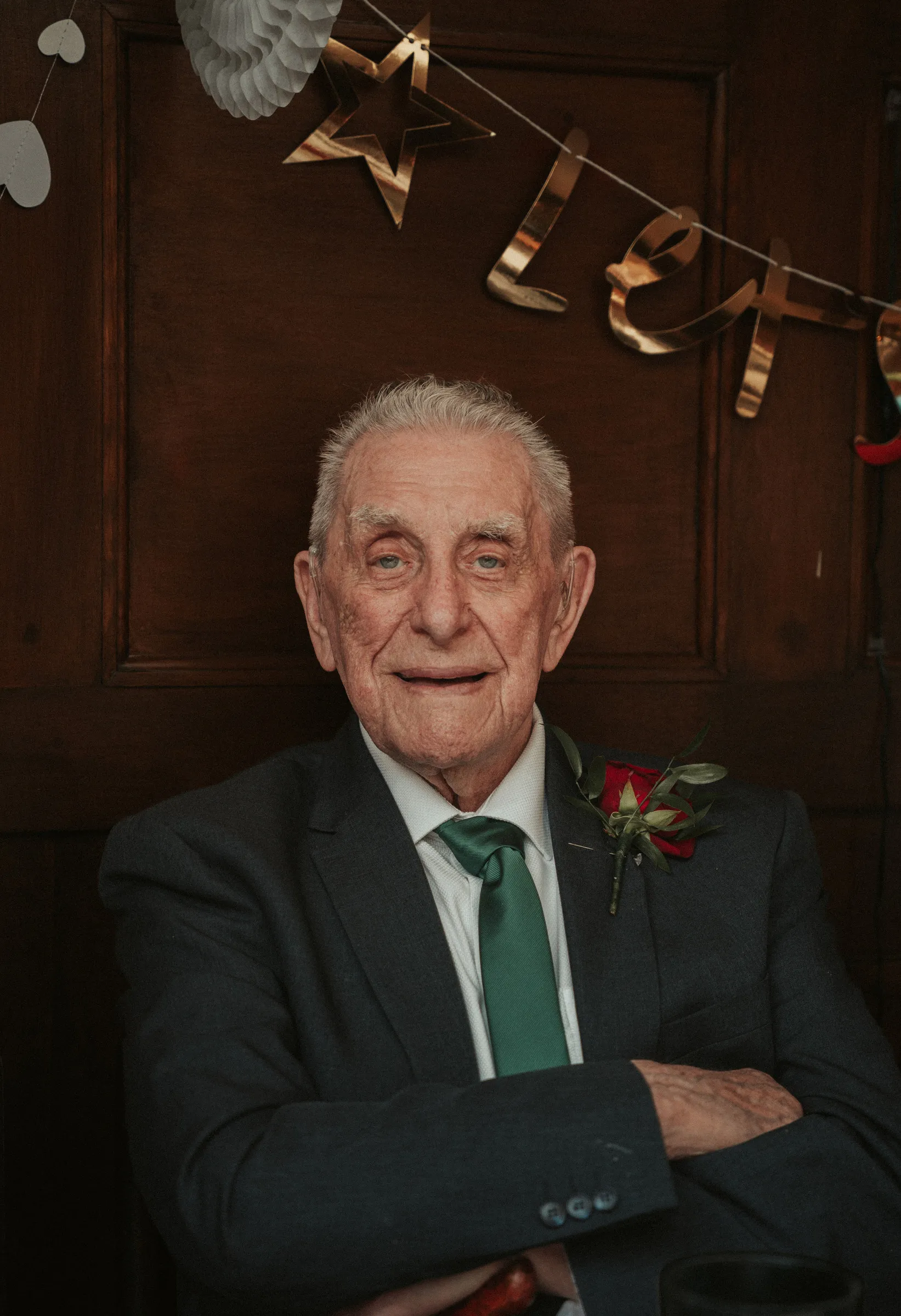 Portrait of a wedding guest in a dark suit and green tie against a panelled wall