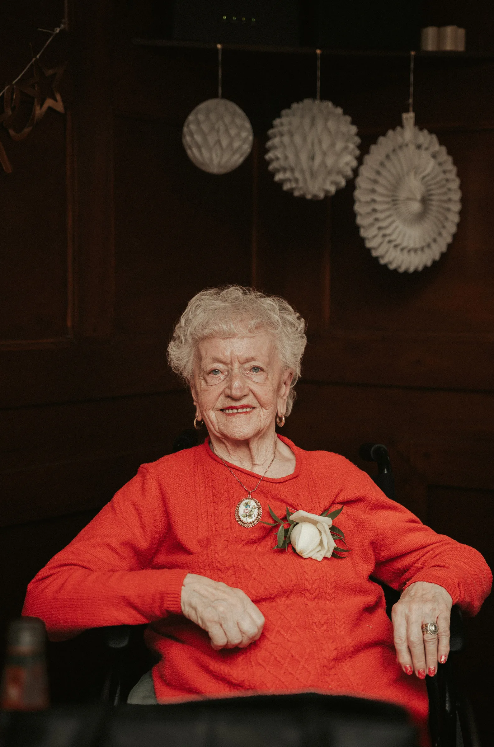 A guest in a red jumper wearing a white rose corsage, seated at the reception