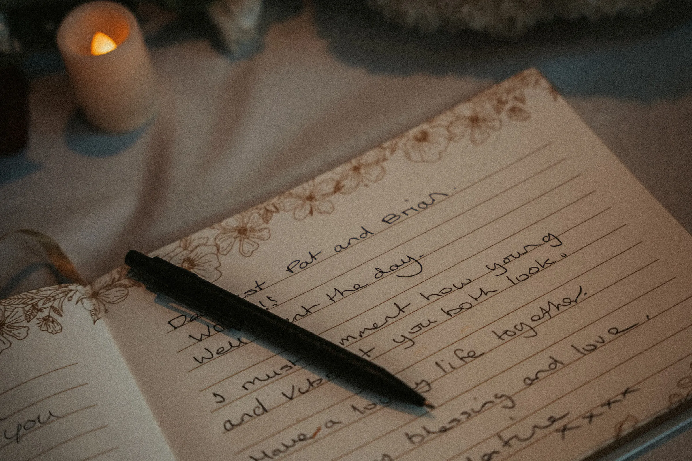 Detail of a handwritten wedding card and fountain pen beside a lit candle
