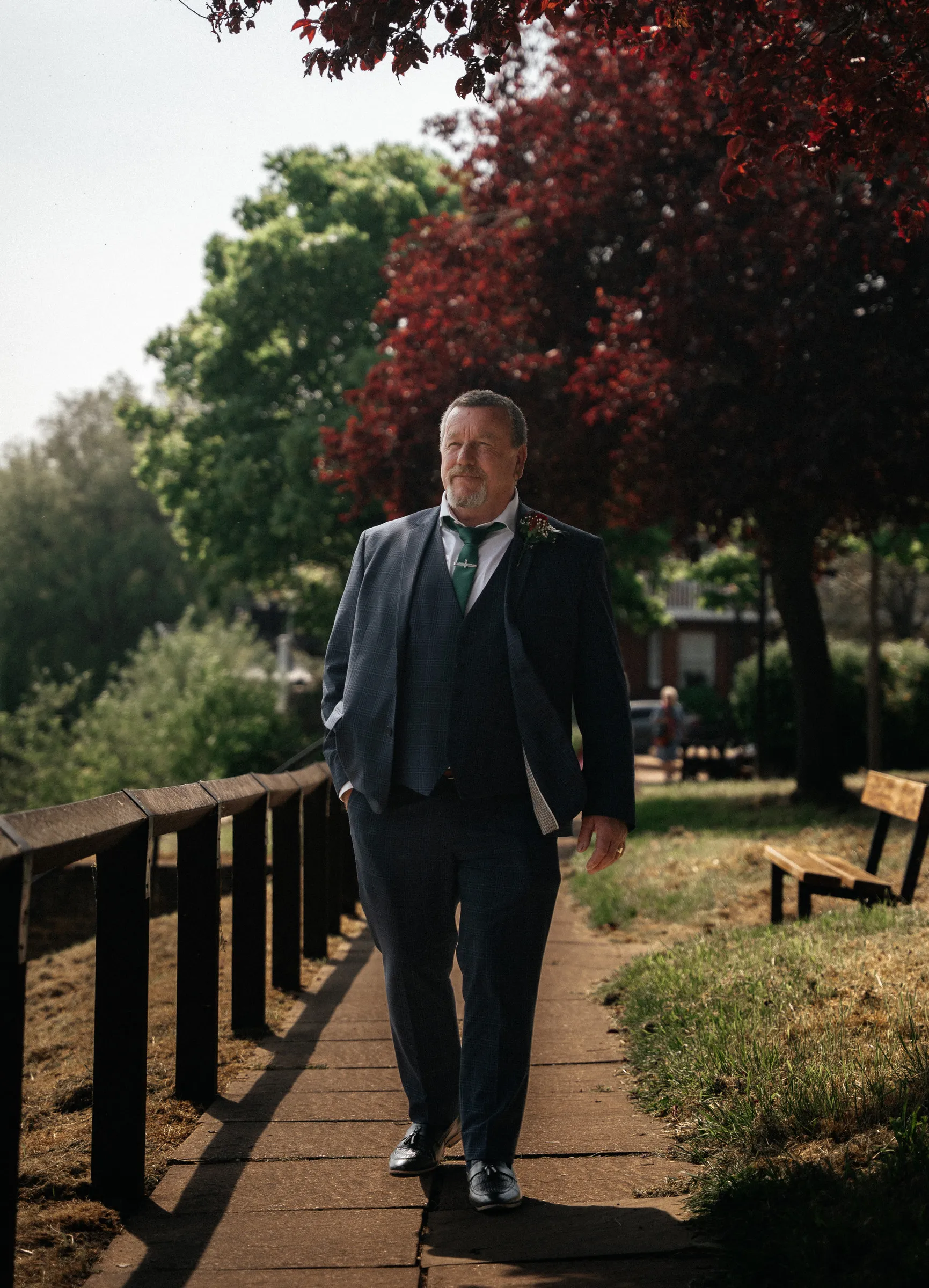 The groom walking along a tree-lined riverside path before the ceremony
