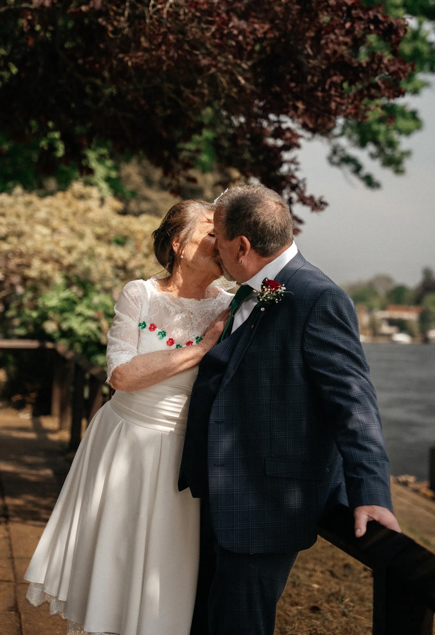 The bride and groom sharing a kiss under an autumn tree by the river