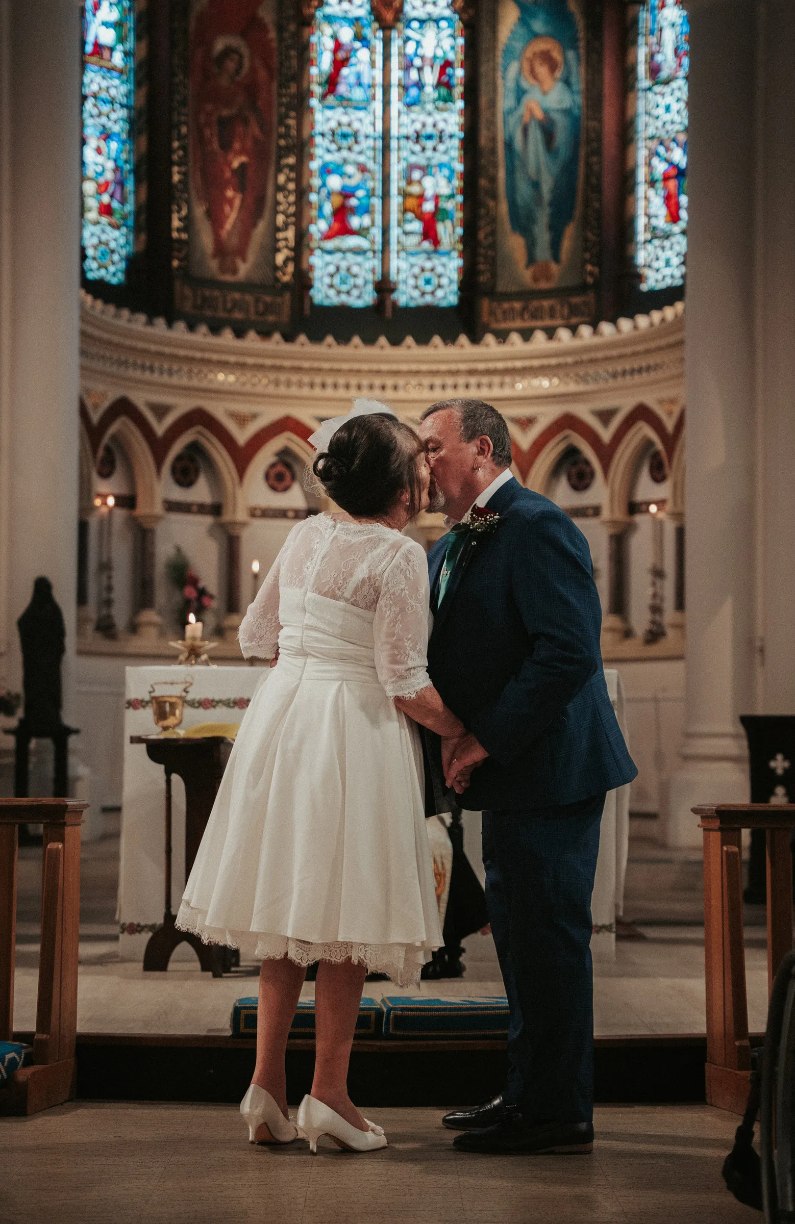 The bride and groom exchanging vows in front of the stained glass window